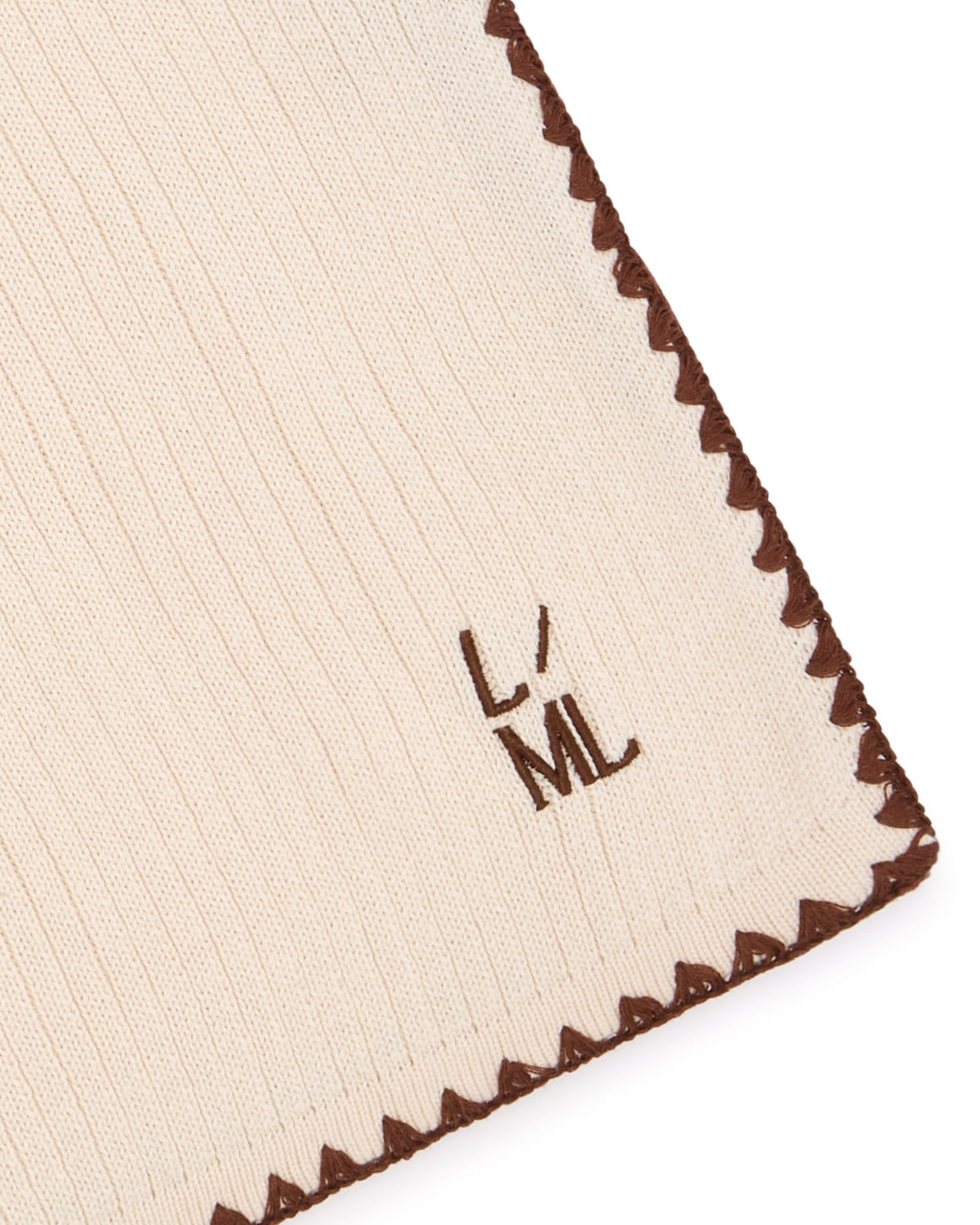 Close-up of the Astor blanket's scalloped edge, ribbed knit and L/ML embroidery